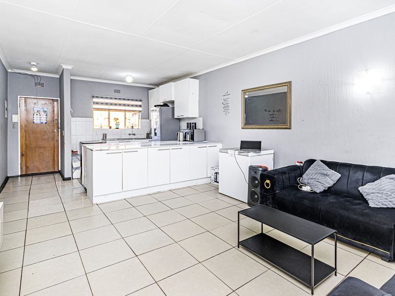 Open-plan living area featuring tiled flooring and a functional kitchen with white cabinetry, providing a versatile space for living and dining.