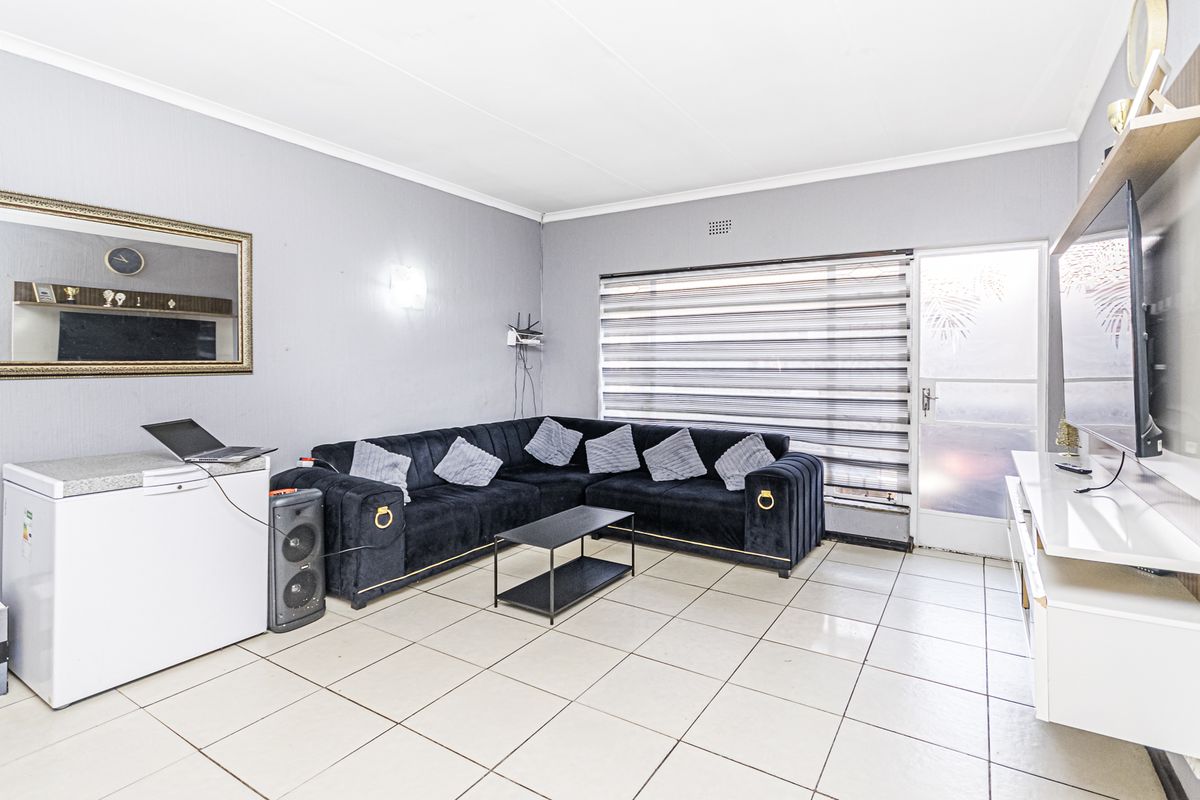 A bright living room featuring neutral tiled flooring, coved ceilings, and a glass panel door leading to the exterior, providing a functional living space.
