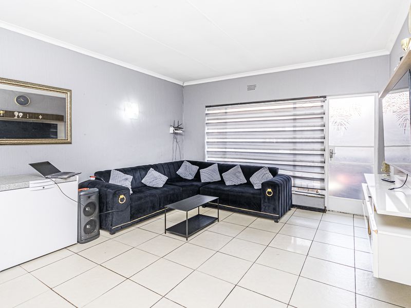 A bright living room featuring neutral tiled flooring, coved ceilings, and a glass panel door leading to the exterior, providing a functional living space.