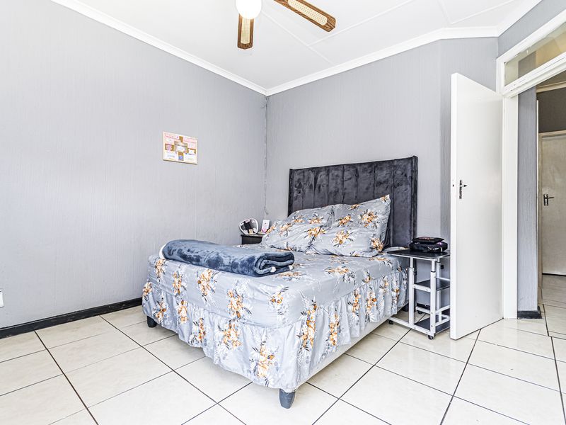 A bedroom featuring tiled flooring, a ceiling fan, and neutral grey walls, providing a functional and well-maintained living space.