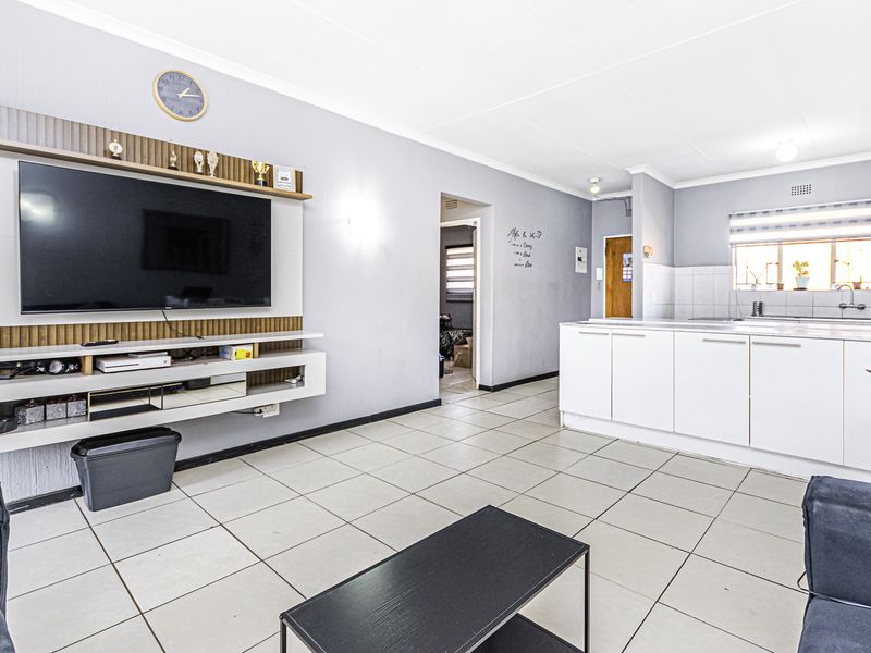 Open-plan living area featuring a modern built-in media unit and a functional kitchen with white cabinetry and tiled flooring.