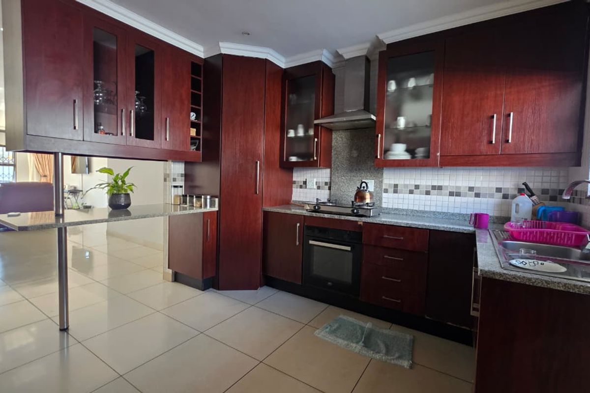 A functional kitchen featuring dark wood cabinetry, granite countertops, built-in oven, gas hob, and a breakfast bar, with tiled flooring throughout.