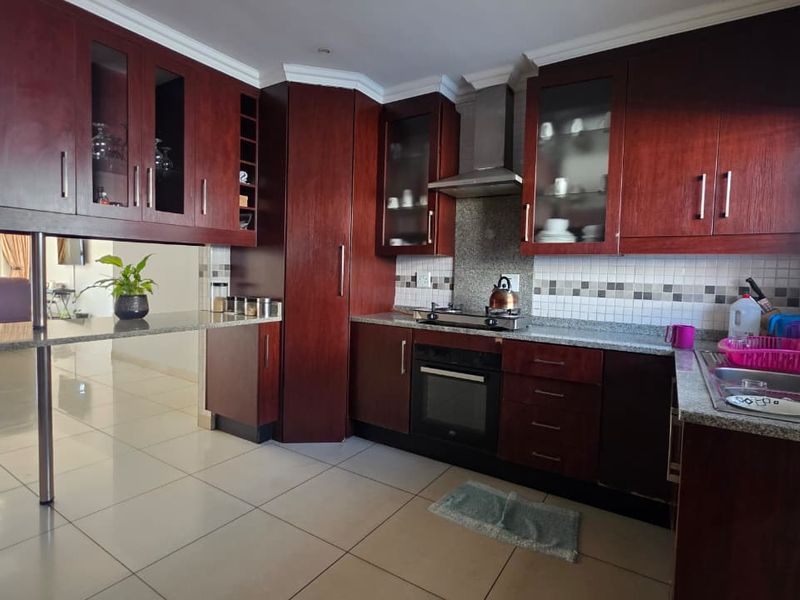 A functional kitchen featuring dark wood cabinetry, granite countertops, built-in oven, gas hob, and a breakfast bar, with tiled flooring throughout.