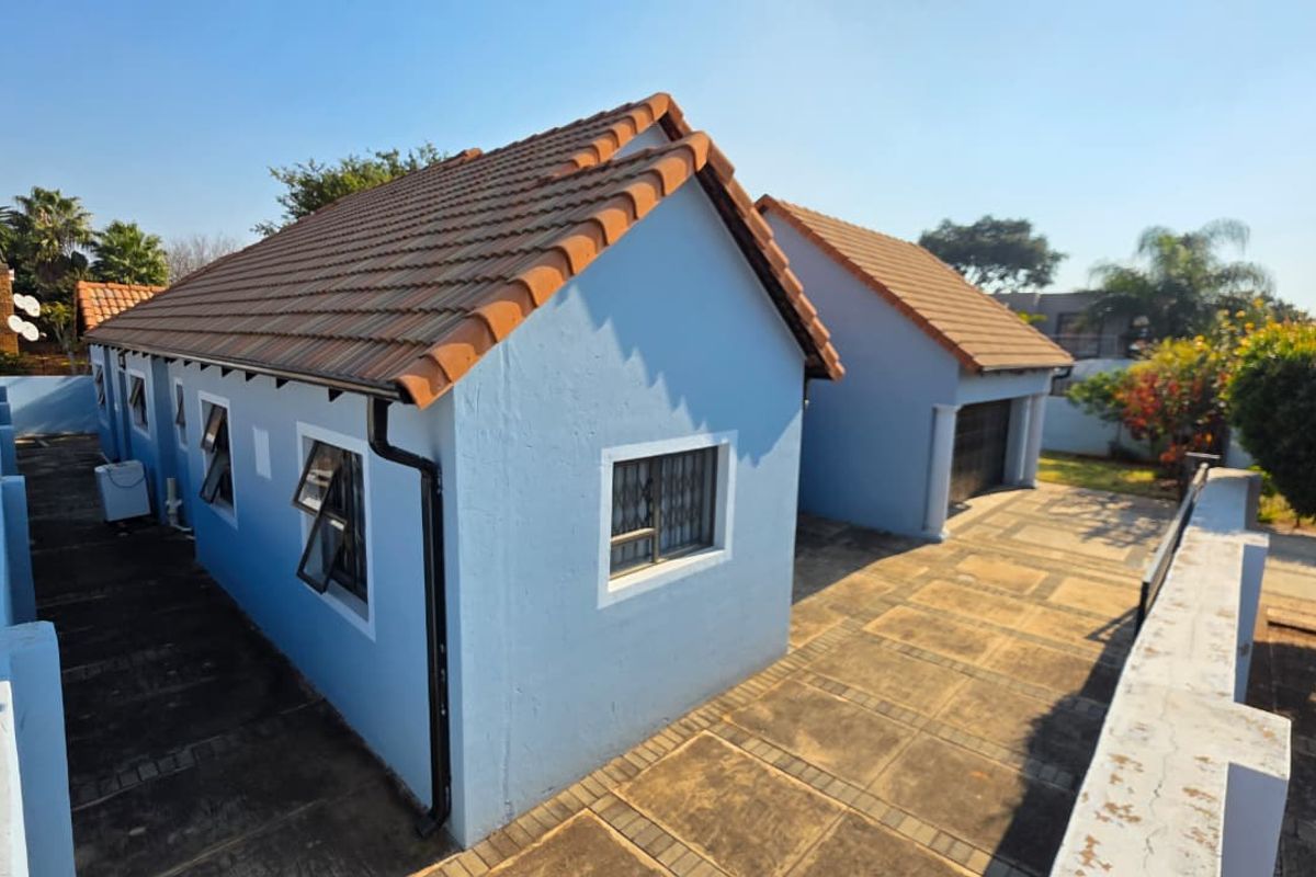 Rear view of the property featuring a tiled roof, paved driveway, and secure garage access.