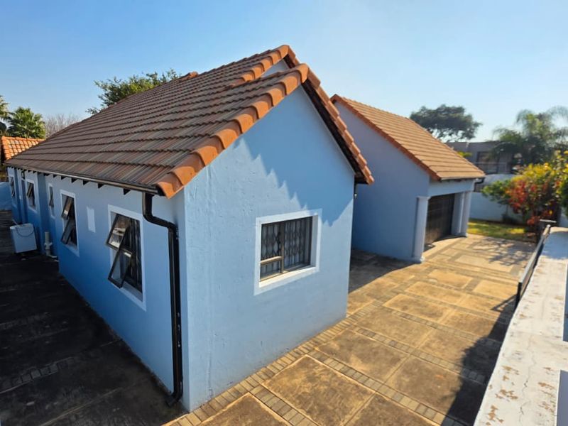 Rear view of the property featuring a tiled roof, paved driveway, and secure garage access.