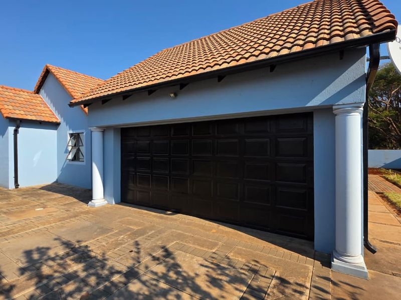 Front view of the property featuring a double garage with a tiled roof, paved driveway, and decorative architectural columns.