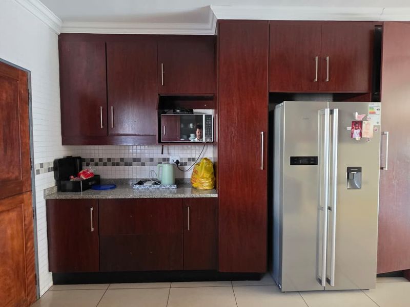 A functional kitchen featuring dark wood cabinetry, granite countertops, a tiled backsplash, and built-in microwave space with tiled flooring throughout.