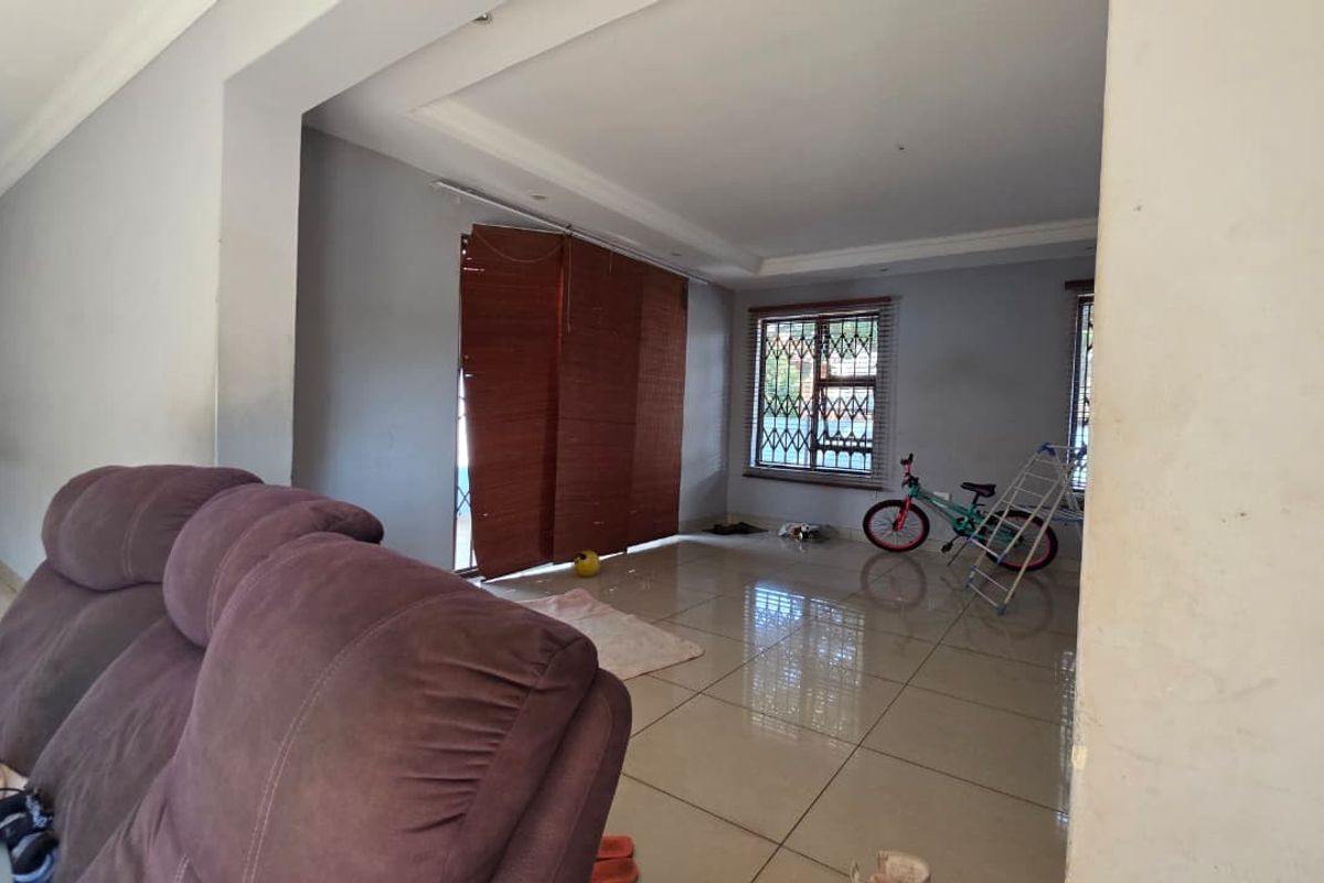 Spacious living area featuring large format floor tiles, recessed ceiling details, and security bars on the windows.