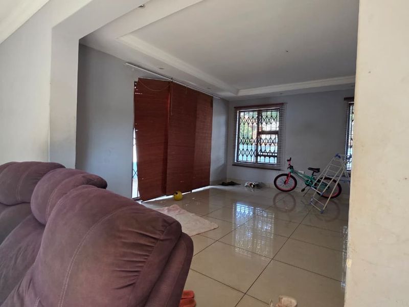 Spacious living area featuring large format floor tiles, recessed ceiling details, and security bars on the windows.