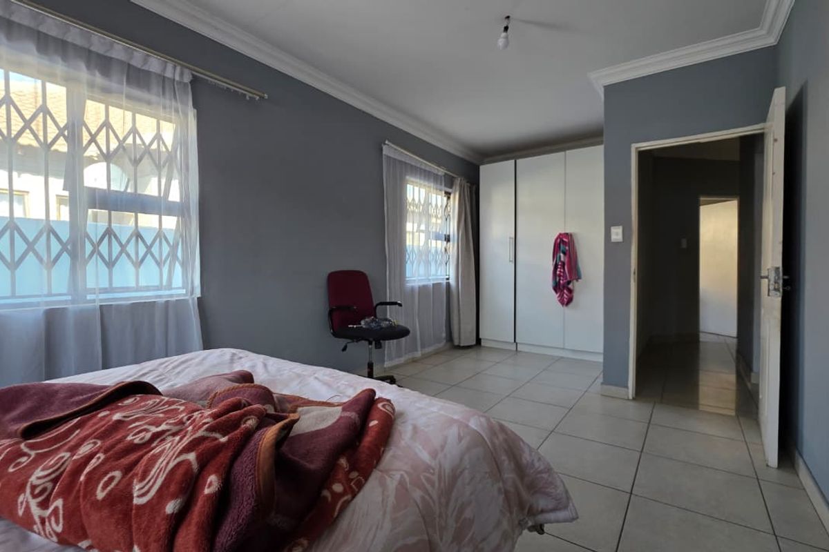 A bedroom featuring tiled flooring, built-in cupboards, and security bars on the windows, offering a functional and neutral living space.