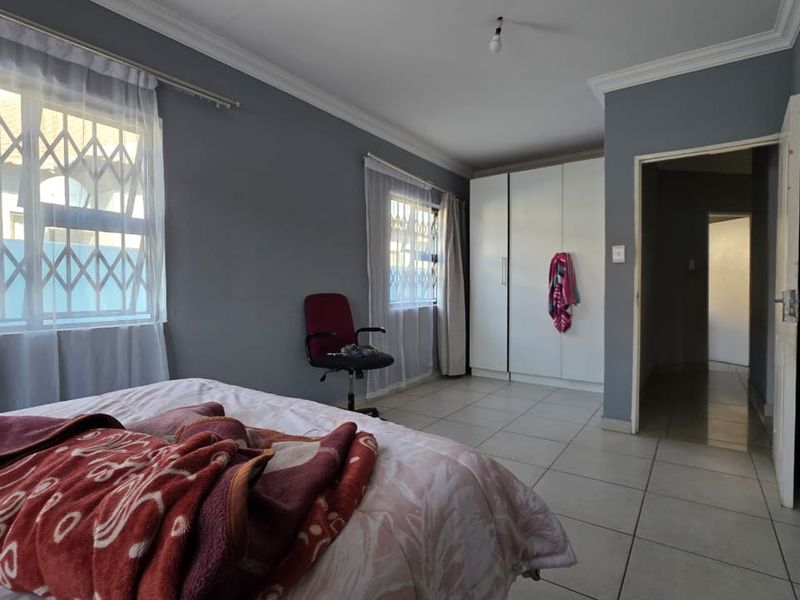A bedroom featuring tiled flooring, built-in cupboards, and security bars on the windows, offering a functional and neutral living space.