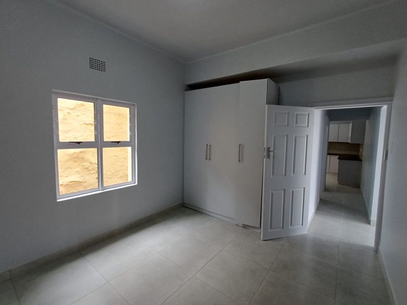 A clean, empty bedroom featuring neutral tiled flooring, built-in cupboards, and an aluminium window, offering a bright and versatile living space.