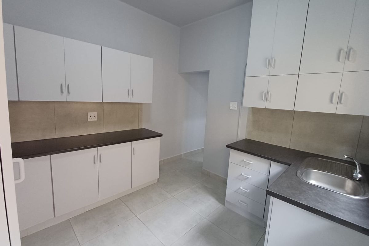 A clean, modern kitchen featuring white cabinetry, dark countertops, a stainless steel sink, and neutral tiled flooring.