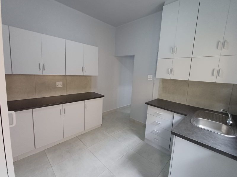 A clean, modern kitchen featuring white cabinetry, dark countertops, a stainless steel sink, and neutral tiled flooring.