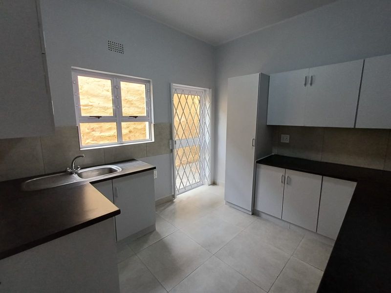 A clean, functional kitchen featuring white built-in cabinetry, dark laminate countertops, tiled flooring, and a secure exterior door.