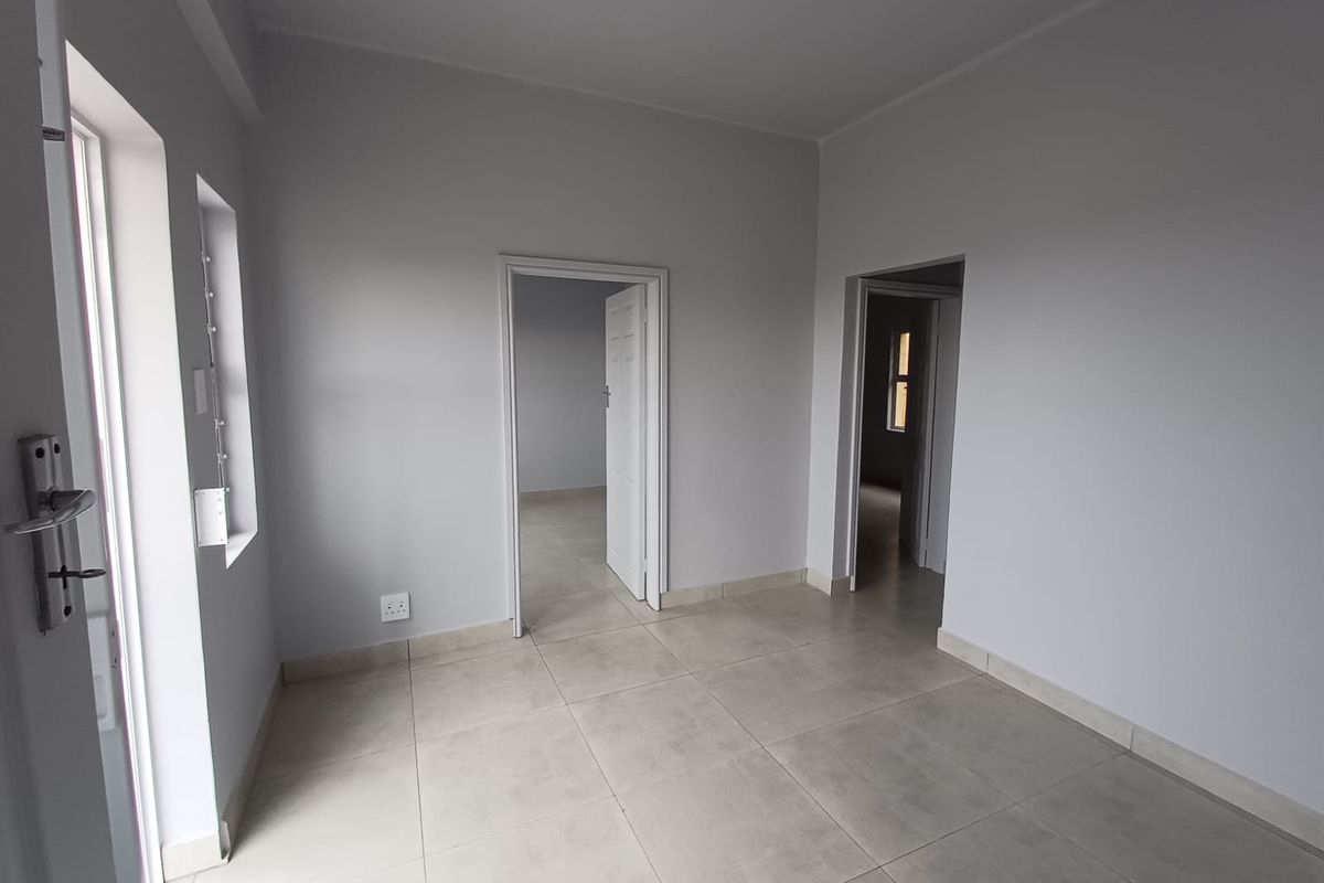 A bright, vacant living area featuring neutral grey walls and modern tiled flooring, providing a clean and versatile space ready for furnishing.