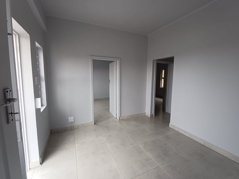 A bright, vacant living area featuring neutral grey walls and modern tiled flooring, providing a clean and versatile space ready for furnishing.