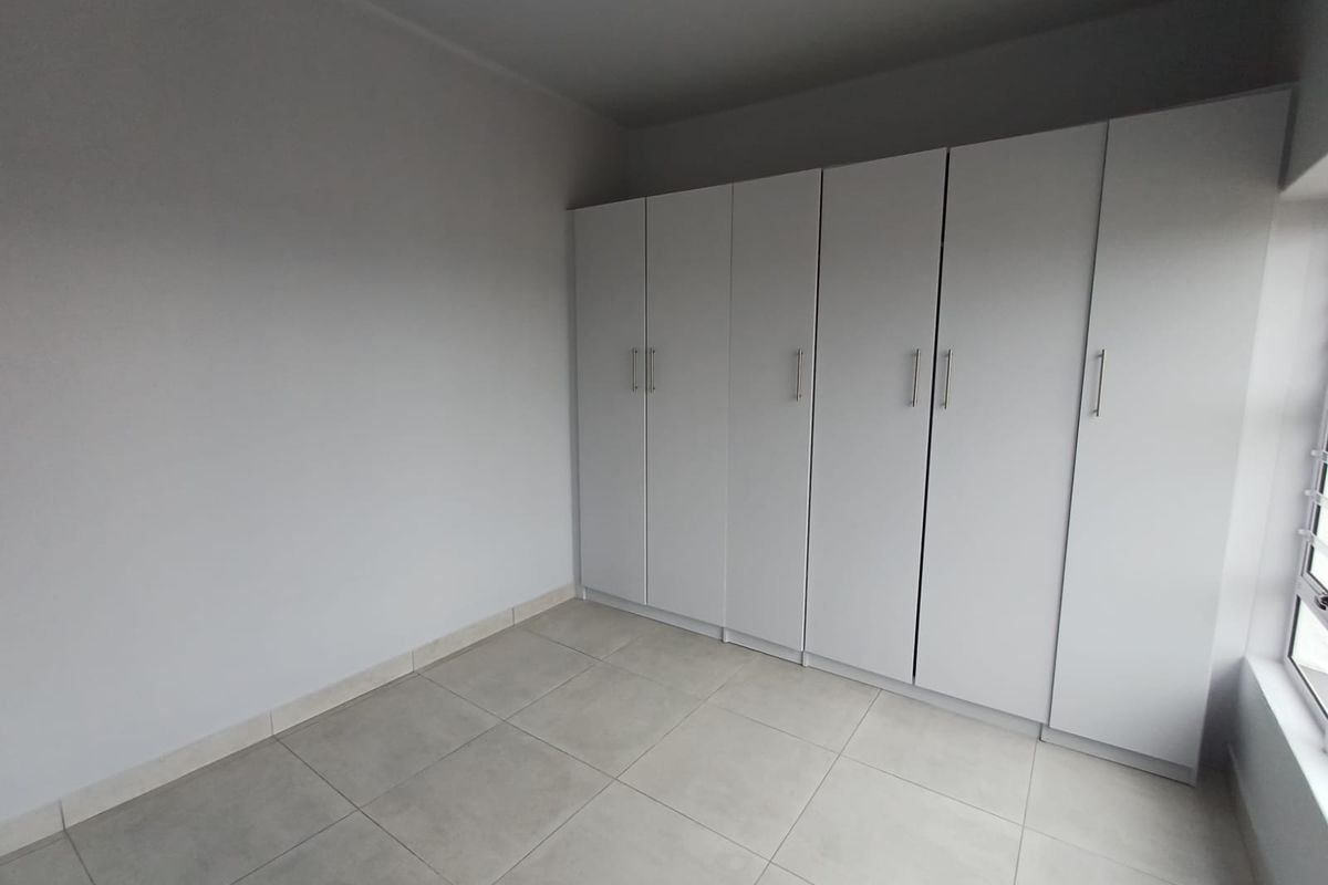 A clean, empty bedroom featuring neutral tiled flooring and extensive white built-in cupboards, offering a versatile space ready for personalization.