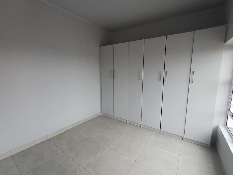 A clean, empty bedroom featuring neutral tiled flooring and extensive white built-in cupboards, offering a versatile space ready for personalization.