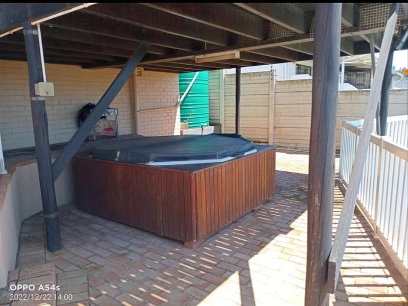 Covered outdoor patio area featuring brick paving and a timber-clad spa, situated beneath an elevated deck structure.