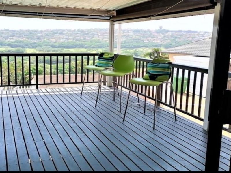 An elevated timber deck balcony featuring a metal balustrade and covered roof structure, offering expansive views of the surrounding landscape.