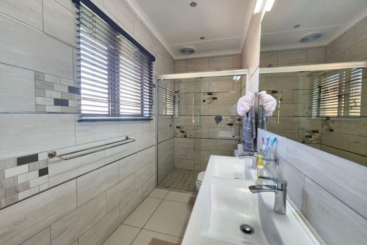 Modern bathroom featuring a double vanity, large wall mirror, and a spacious glass-enclosed shower with contemporary tiled finishes.