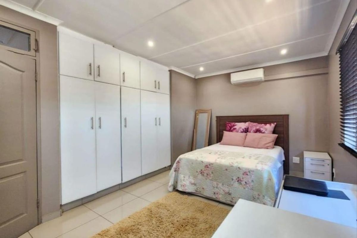 A well-maintained bedroom featuring neutral wall tones, tiled flooring, ample built-in cupboard storage, and a wall-mounted air conditioning unit.