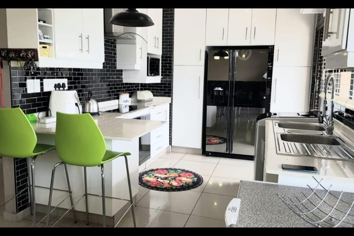 Modern kitchen featuring white cabinetry, stone countertops, black subway tile backsplash, and integrated appliances with a breakfast bar area.