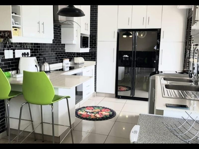Modern kitchen featuring white cabinetry, stone countertops, black subway tile backsplash, and integrated appliances with a breakfast bar area.