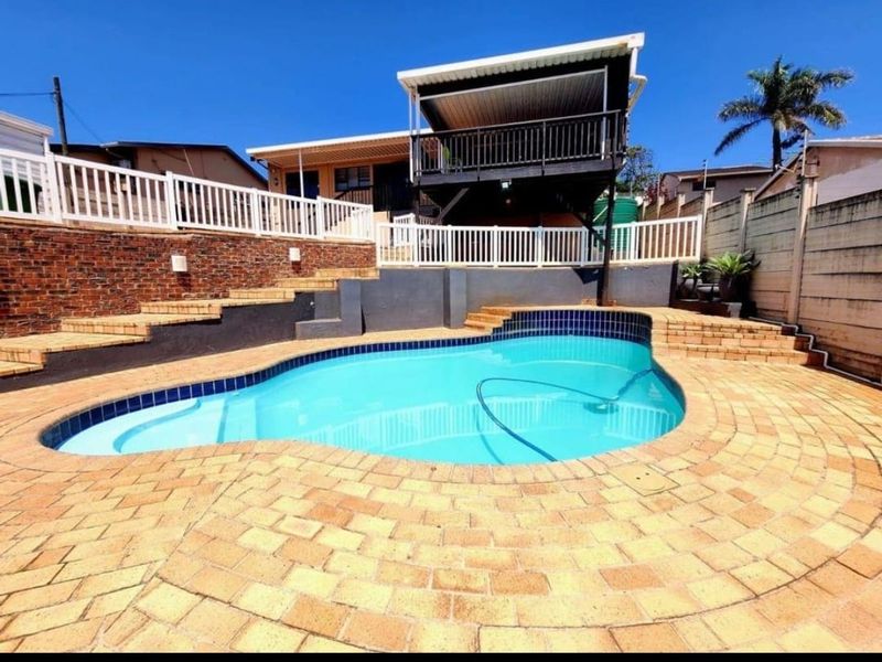 Outdoor pool area featuring a swimming pool, brick paved surround, tiered retaining walls, and an elevated wooden deck with a balustrade.