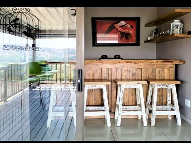 A compact indoor bar area featuring a rustic wooden counter, floating shelves, and large sliding glass doors opening onto an outdoor balcony.