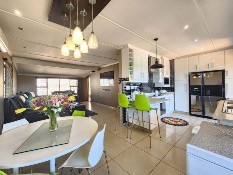 Modern open-plan living area featuring a well-appointed kitchen with island, sleek cabinetry, subway tile backsplash, and integrated lighting, flowing into a comfortable lounge space.