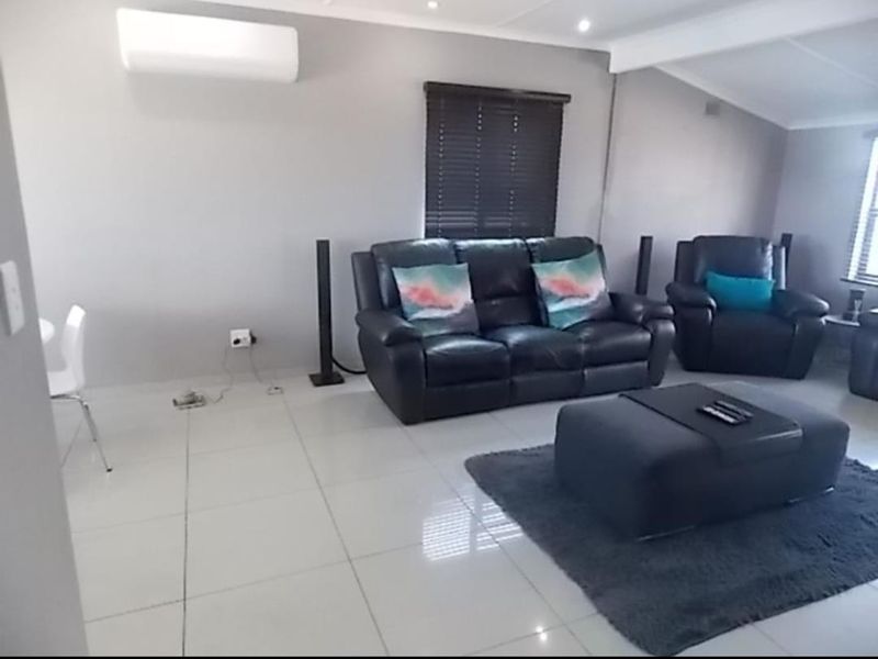 A bright and spacious living room featuring neutral tiled flooring, recessed downlighting, and a wall-mounted split-system air conditioner.