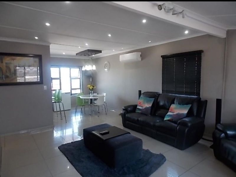 An open-plan living and dining area featuring tiled flooring, recessed downlighting, and a wall-mounted split-system air conditioner.