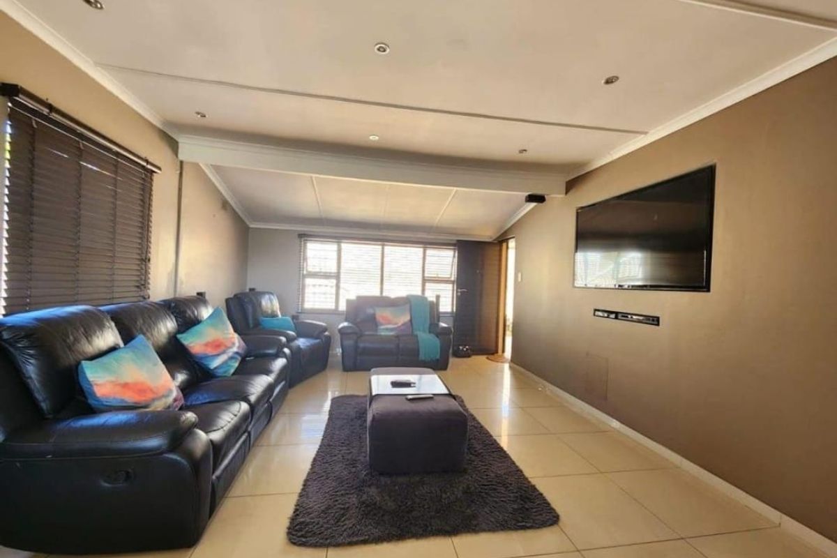 A spacious living room featuring tiled flooring, recessed ceiling lights, and large windows with venetian blinds, providing a comfortable and functional family area.