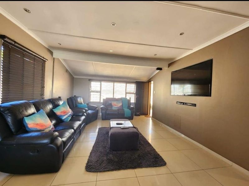 A spacious living room featuring tiled flooring, recessed ceiling lights, and large windows with venetian blinds, providing a comfortable and functional family area.