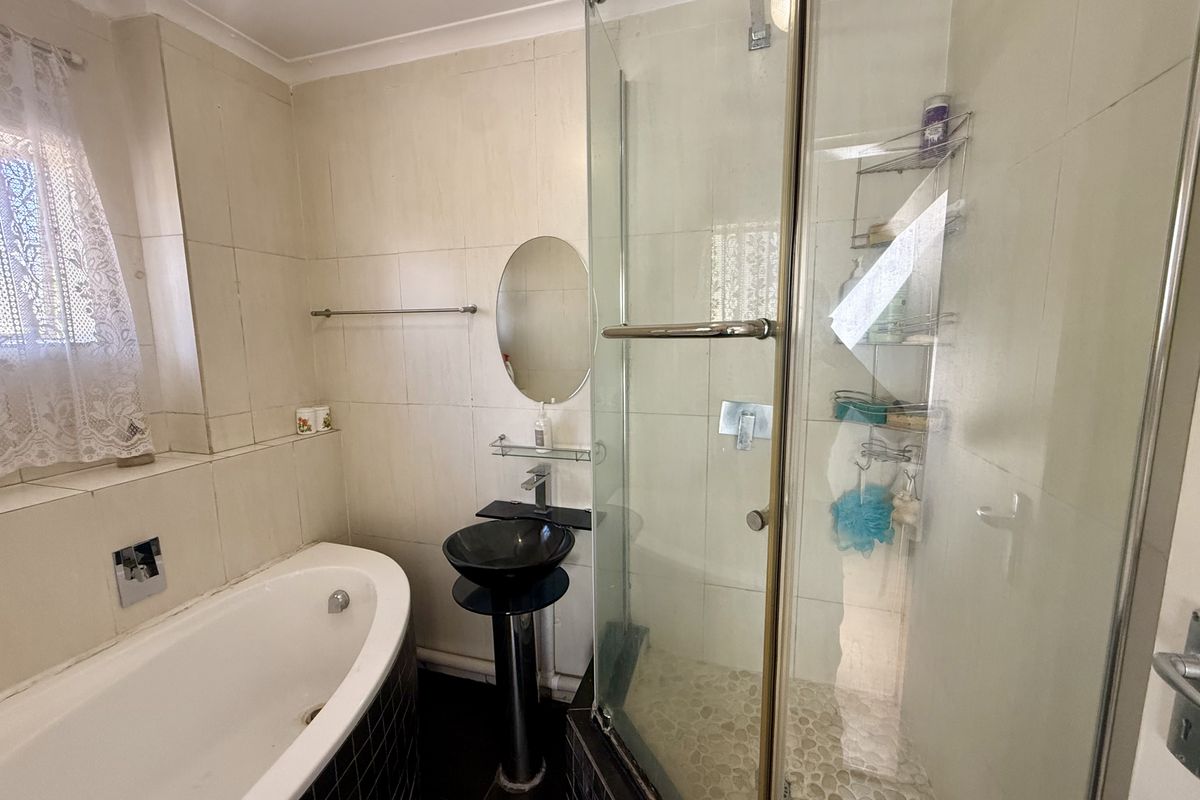 A functional bathroom featuring a bathtub, a separate glass-enclosed shower, and a modern pedestal basin with neutral wall tiling.