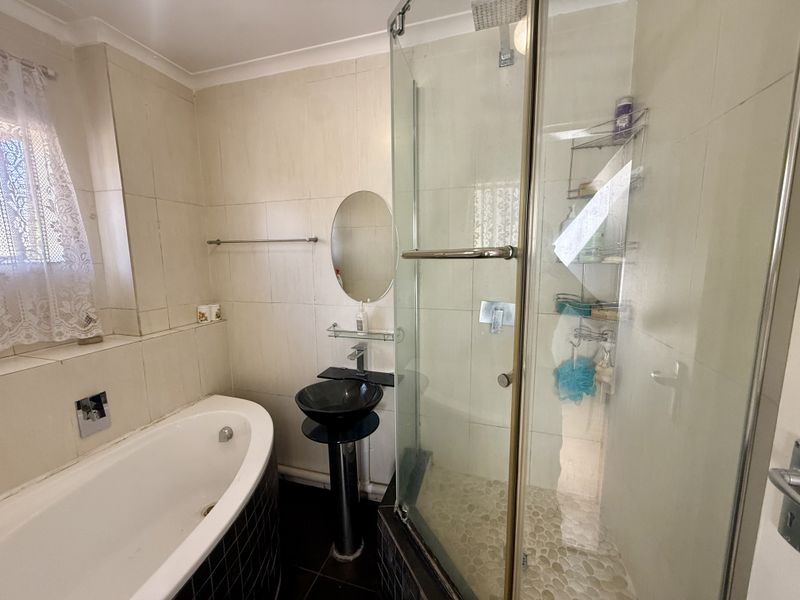 A functional bathroom featuring a bathtub, a separate glass-enclosed shower, and a modern pedestal basin with neutral wall tiling.