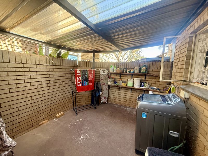 Covered outdoor laundry area featuring brick walls, fixed wall-mounted shelving, and plumbing connections for a washing machine.