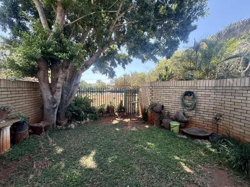 A private rear garden area featuring a brick boundary wall, mature tree, and a metal security gate leading to the exterior.