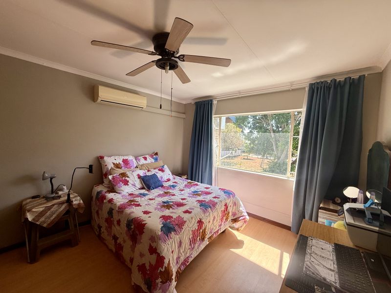 A well-lit bedroom featuring laminate flooring, a ceiling fan, and a wall-mounted split-system air conditioner, offering a comfortable and functional living space.