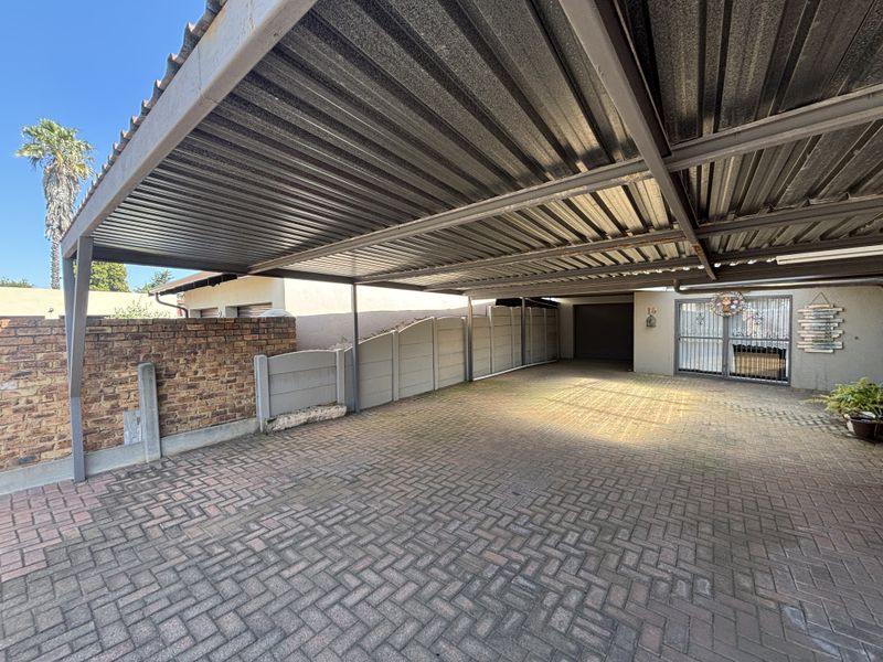 A spacious covered carport area featuring brick paving, a metal roof structure, and secure boundary walls.