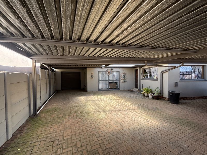 A covered carport area featuring a corrugated metal roof, paved driveway, and secure access to the main entrance and garage.