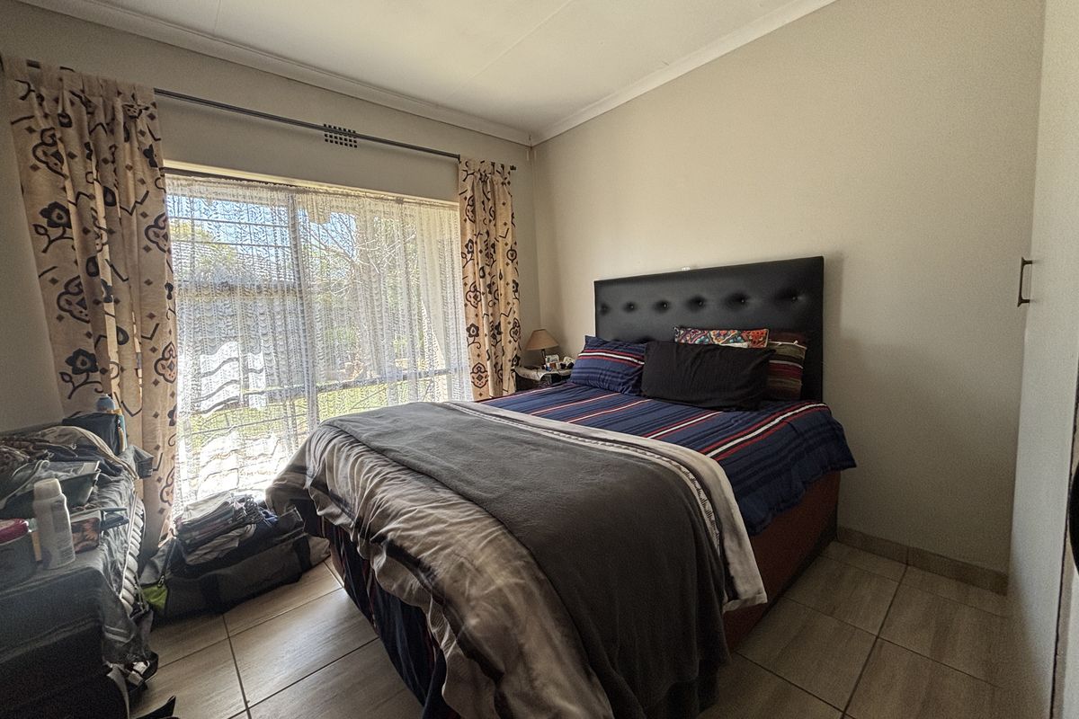 A bedroom featuring tiled flooring, a built-in cupboard, and a sliding glass door providing natural light and garden access.