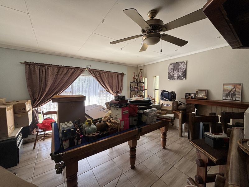 Living room featuring tiled flooring, a ceiling fan, and a brick fireplace, currently used as a storage area.