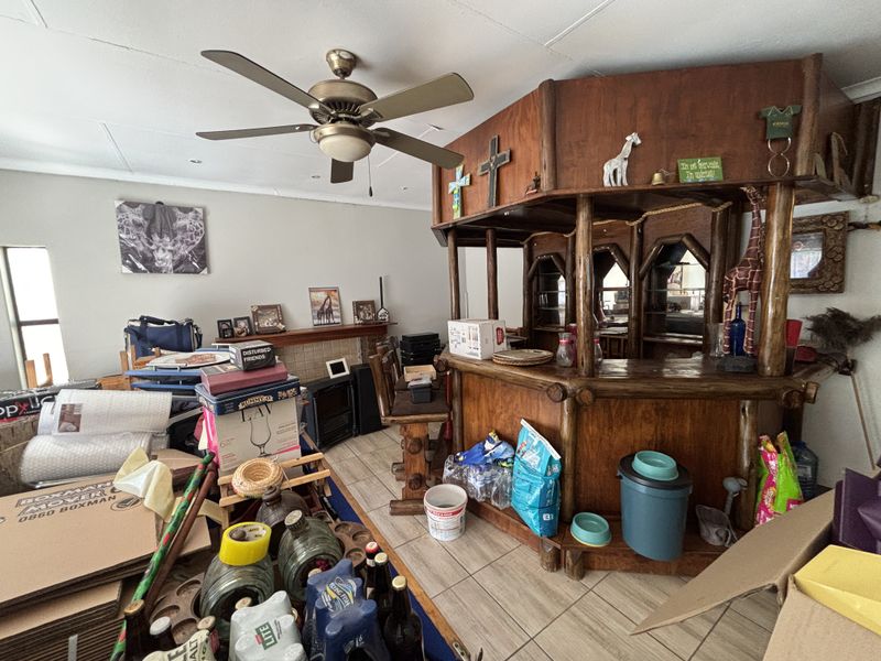A dedicated bar area featuring a built-in wooden counter, ceiling fan, and tiled flooring, currently used for storage.