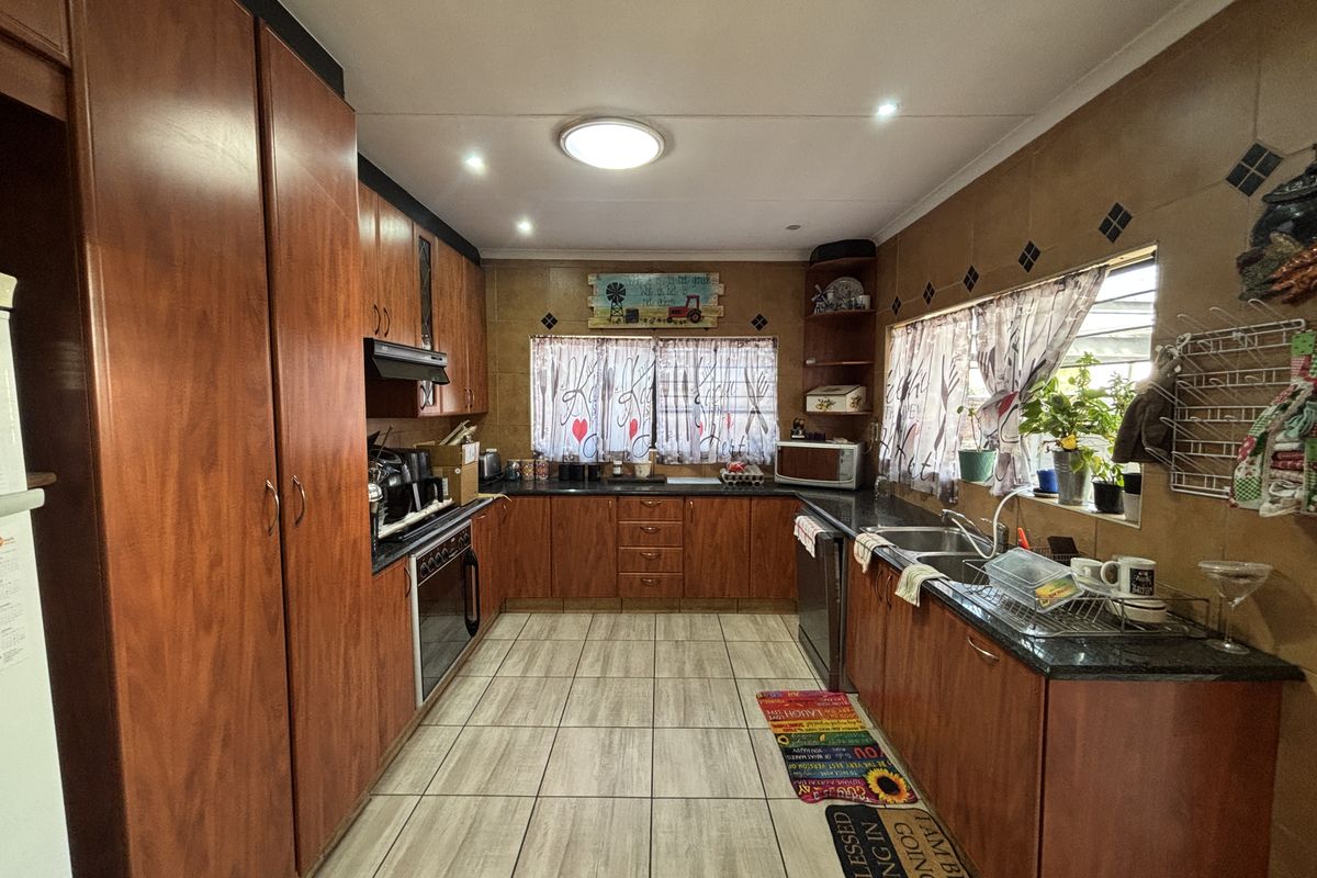 A functional kitchen featuring extensive wood-finish cabinetry, dark countertops, a double basin sink, and tiled flooring with a classic layout.