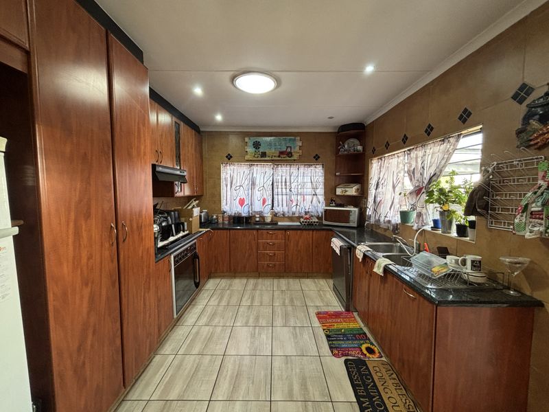 A functional kitchen featuring extensive wood-finish cabinetry, dark countertops, a double basin sink, and tiled flooring with a classic layout.