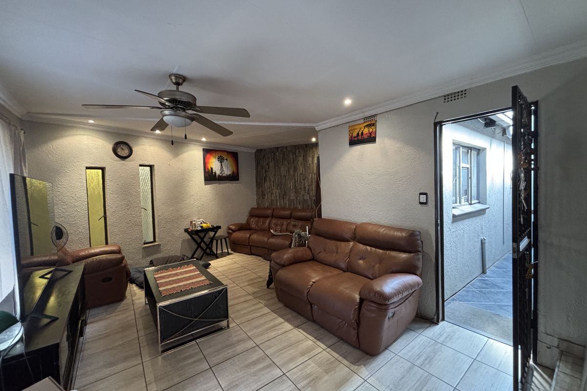 A living room featuring tiled flooring, a ceiling fan, and a stone feature wall, with direct access to an exterior walkway.