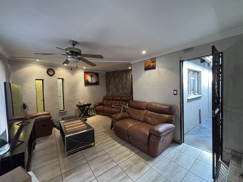 A living room featuring tiled flooring, a ceiling fan, and a stone feature wall, with direct access to an exterior walkway.